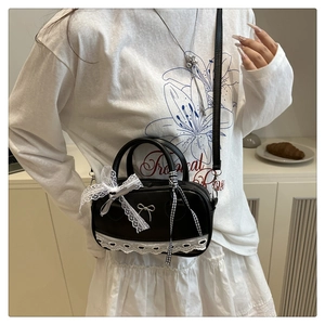 Detail of black faux leather Boston bag with white lace trim and silver bow metallic buckle