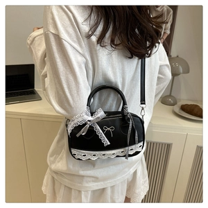Detail of a black ballet-style Boston bag with white lace trim and metallic bow logo