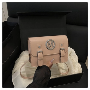 Detail of pink messenger bag with metallic M emblem and dual straps on white satin