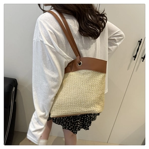 Detail view of straw tote bag with brown leather handles worn by model in casual setting