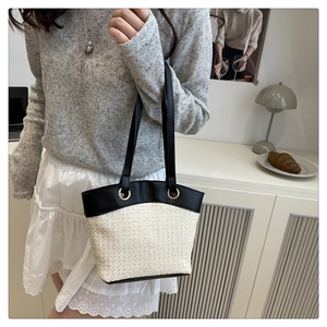 Woman carrying large bicolor straw tote bag with black leather straps in casual home setting