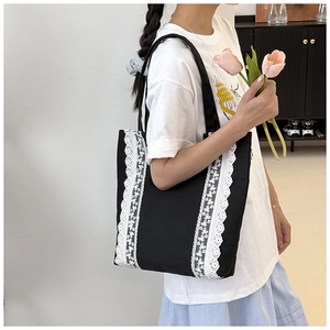 Détail d'un sac cabas en toile noire avec dentelle blanche porté par un mannequin