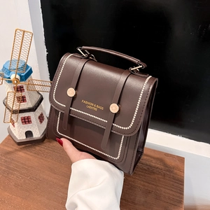 Retro dark brown leather handbag with gold buckle and white stitching on wooden desk