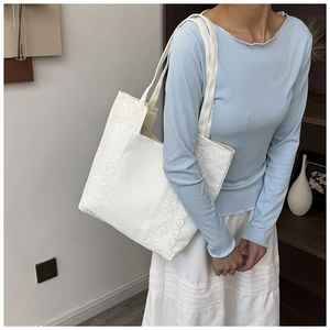 Vue détaillée d'un sac cabas en toile blanche avec bordures en dentelle et détails floraux