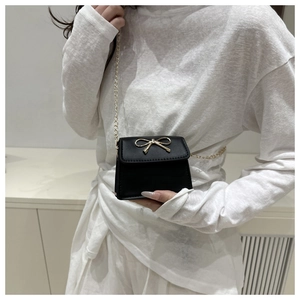 Close-up of a mini black leather crossbody bag with a golden bow-shaped metal clasp