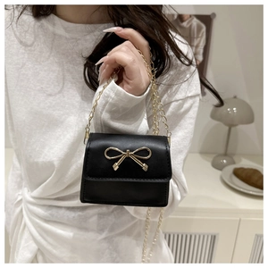 Dettaglio dell'elegante mini borsa a sella nera con fiocco dorato in una scena lifestyle