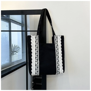 Gros plan sur un cabas en toile noire avec des motifs de fleurs en dentelle blanche