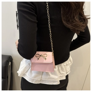 Pink mini crossbody bag featuring a golden bow buckle and chain strap on a model