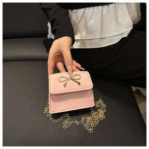 Dettaglio della mini borsa a sella rosa con chiusura a fiocco dorato e catena