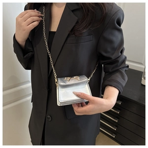 Close-up of silver mini square bag featuring a gold bow accent and fine chain strap