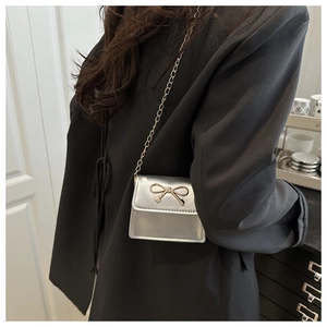 Silver bow saddle bag with gold chain strap worn over a black blazer for chic style