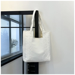 Détail d'un sac cabas en toile blanche avec bordure en dentelle suspendu à une porte