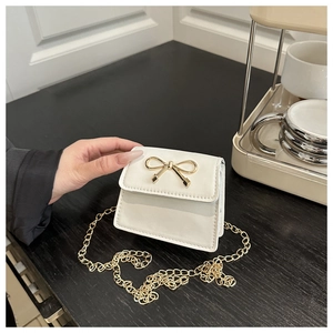 Dettaglio della mini borsa a sella bianca con fibbia a fiocco dorata e tracolla a catena