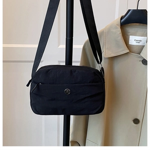 Close-up of black crossbody bag with metal M logo and wide nylon strap detail
