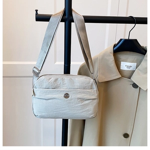 Close-up of light grey nylon crossbody bag with adjustable wide strap and metal logo