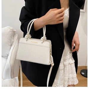 Detail of white crocodile pattern handbag with gold fashion text and knotted handle