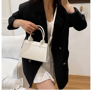 Detail of white crocodile pattern handbag with unique knot handle and gold fashion text