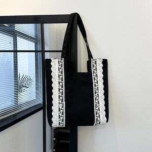 Grand sac cabas noir en toile avec dentelle blanche suspendu devant une fenêtre