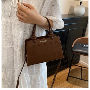 Detail of dark brown crocodile embossed crossbody bag with knotted handle and gold text