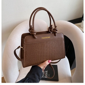 Detail of brown crocodile pattern handbag with knotted handle and golden branding