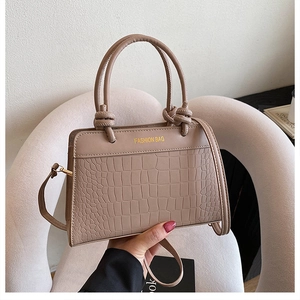 Detail of crocodile embossed leather texture and gold knot handle on a mini handbag
