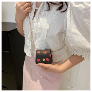 Close-up of mini black crossbody chain bag with red strawberry print and gold hardware