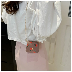 Mini strawberry print crossbody bag with gold chain strap worn on a white lace top
