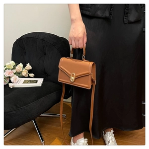 Close-up of a brown leather shoulder bag featuring a gold oval twist-lock on black dress
