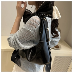 Detail of black glossy shoulder bag featuring silver rivets and a large bow design