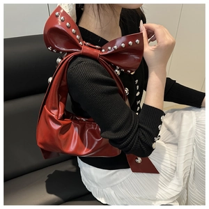 Macro detail of wine red underarm bag with oversized bow and silver metal rivets