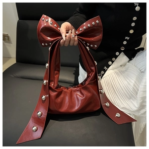 Close-up of wine red leather bow bag with silver studs on a dark grey sofa