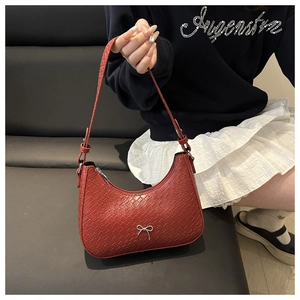 Close-up of woven dark red shoulder bag with silver metal bow and adjustable strap