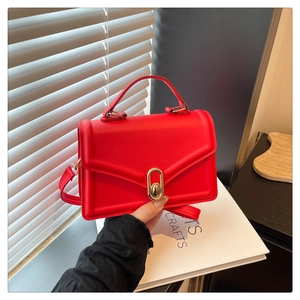 Détail d'un sac à bandoulière en cuir mat rouge avec fermoir doré et poignée supérieure