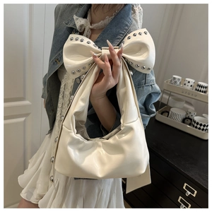 Detail of white glossy leather bow handle with silver metal studs on a crescent bag