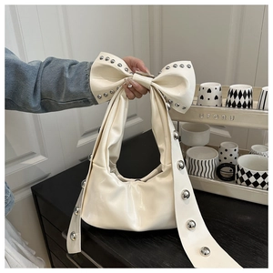 Detailed close-up of cream bow shoulder bag with silver studs held by a model