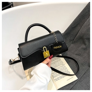 Detail of black leather crossbody bag with golden lock on a grey suit background