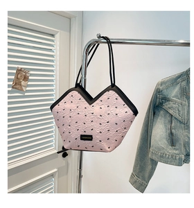 Detail of pink tote bag with black bow patterns hanging on a metal rack in a room