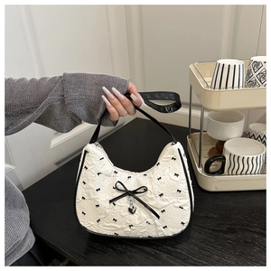 Detail of white crescent bag with black bow patterns and silver heart pendant charm