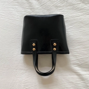 Detail of black leather bucket bag with gold metal rivets and minimalist handle design