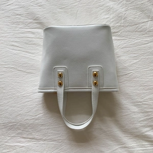 Close-up of white bucket bag texture with gold spherical studs and premium PU leather