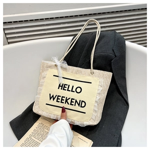 Detail of straw tote bag featuring Hello Weekend print, white lace trim and rope handle