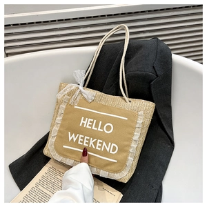 Detail of woven straw tote bag with Hello Weekend print and white lace bow decoration