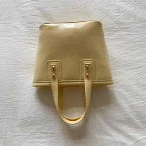 Vertical top view of a light yellow leather bucket bag with gold rivets on handles