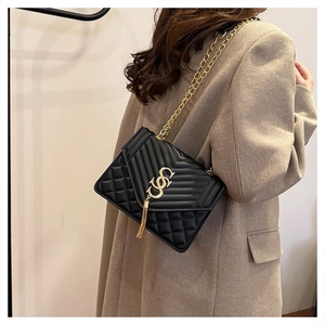 Detail of black quilted leather crossbody bag with gold tassel and elegant metal chain strap