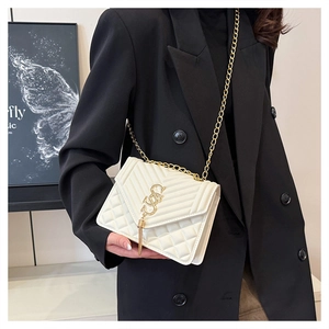 White quilted chain shoulder bag with gold logo and tassel on a chic black outfit
