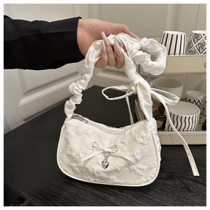 Detalle del bolso blanco con jacquard floral y un colgante de corazón plateado