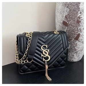 Detail of black crossbody bag with V-quilt pattern, gold logo and metal tassel pendant