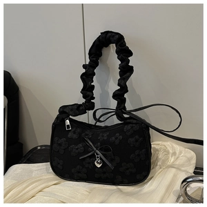 Detalle de textura floral en bolso negro con colgante de corazón y asa con volantes