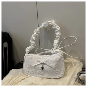 Detalle de bolso blanco con textura floral en relieve y colgante de corazón de metal