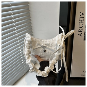 Detalle de bolso plisado blanco con textura de encaje floral y colgante de corazón